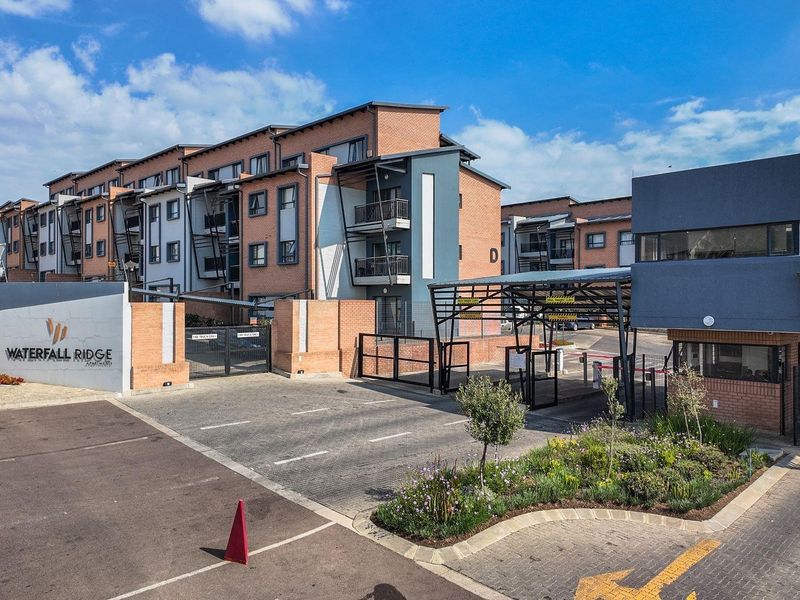 The main entrance and security gatehouse of Waterfall Ridge apartment complex, featuring modern brick architecture and well-maintained landscaped grounds.