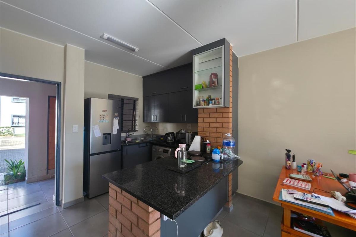 A functional kitchen featuring dark cabinetry, granite countertops, and an exposed brick breakfast bar, with tiled flooring and direct access to the hallway.