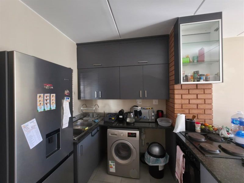 Compact kitchen featuring dark grey cabinetry, granite countertops, an electric hob, built-in oven, and a distinctive exposed brick feature wall.