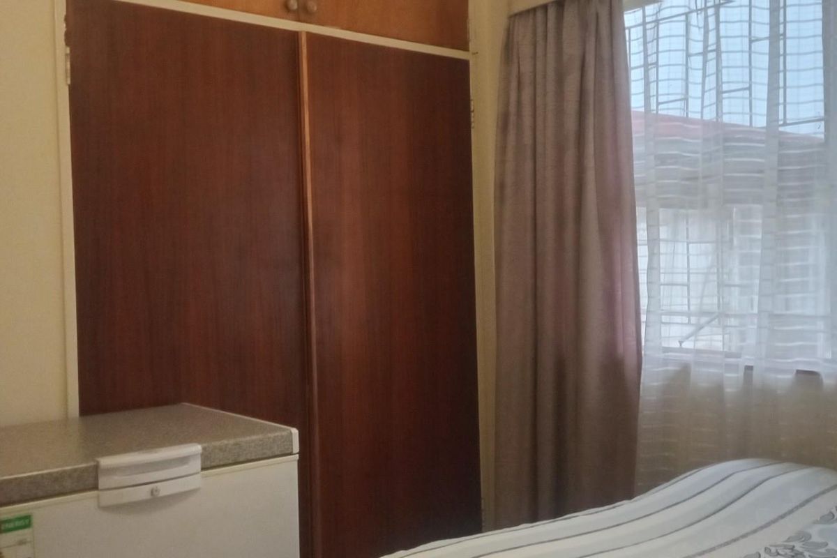 A bedroom featuring built-in wooden cupboards and a window fitted with security bars.