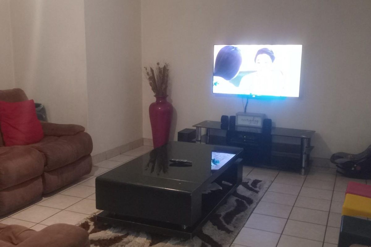 A living room featuring tiled flooring and a wall-mounted television setup.