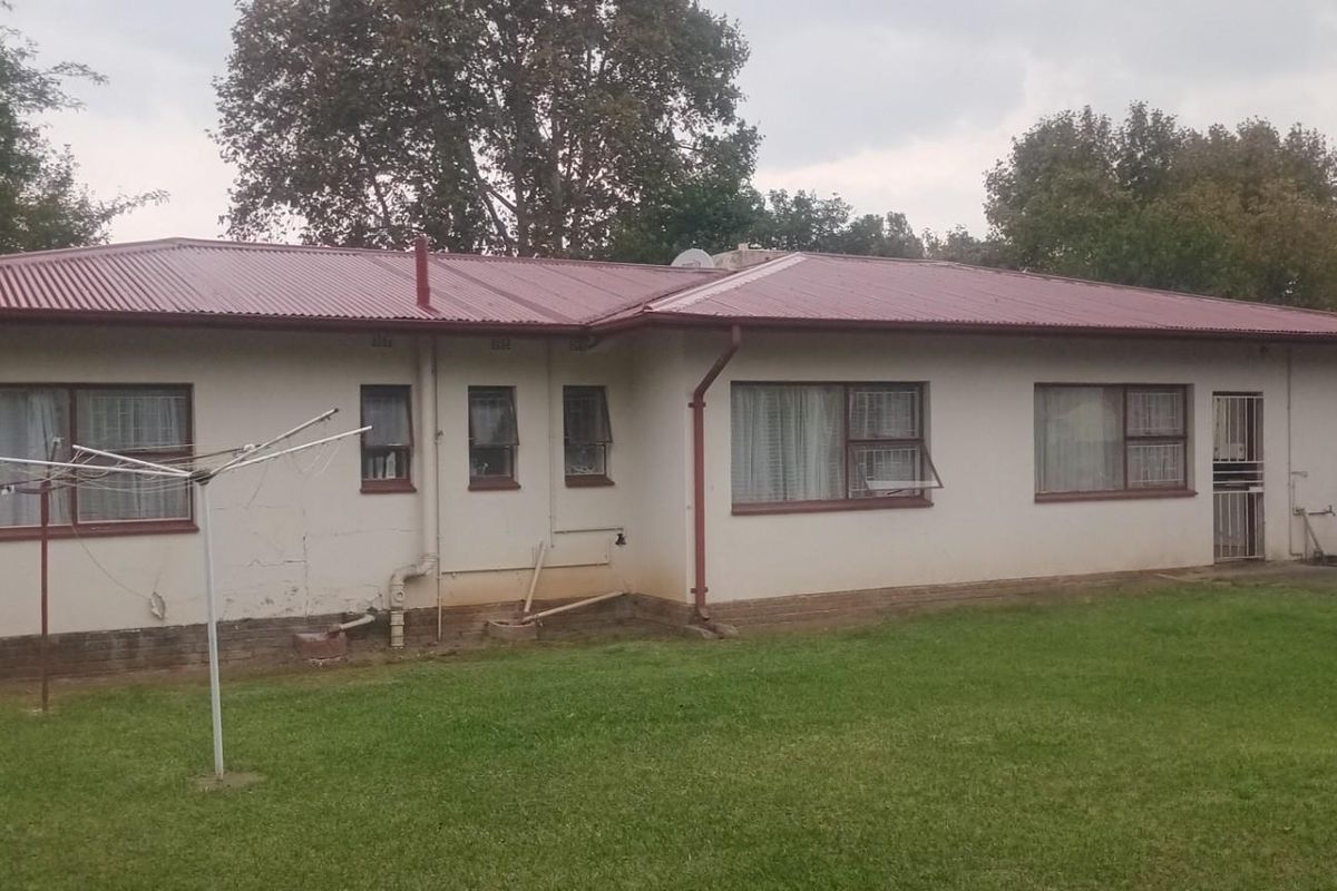 Rear view of a single-story house featuring a corrugated metal roof, exterior wall plastering, and a surrounding lawn area.