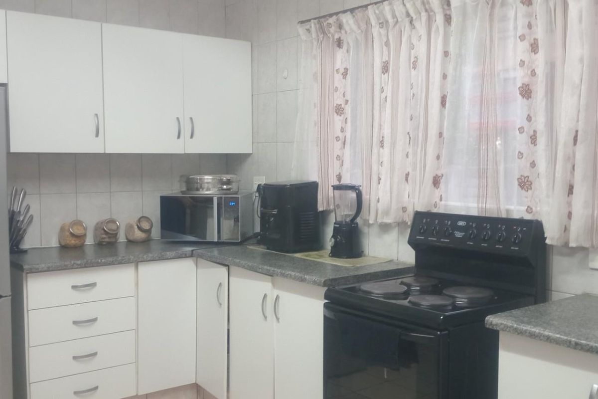 A functional kitchen featuring white cabinetry, laminate countertops, tiled backsplash, and a freestanding electric stove.