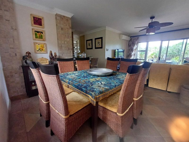Open-plan living and dining area featuring tiled floors, a stone-clad feature pillar, ceiling fan, and sliding glass doors leading to the outdoor space.