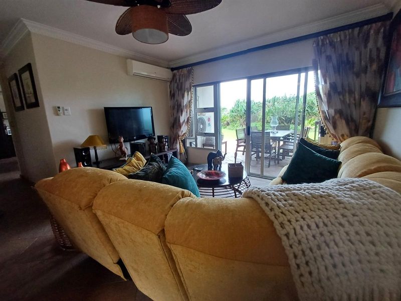 A comfortable living room featuring tiled flooring, crown molding, a ceiling fan, and split-system air conditioning, with direct access to an outdoor patio area.