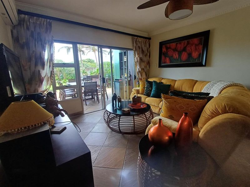 A comfortable living room featuring tiled floors, a ceiling fan, and large sliding glass doors that provide direct access to an outdoor patio area.