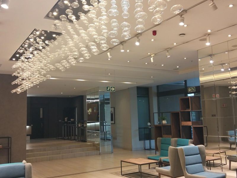 A modern, spacious lobby or clubhouse area featuring contemporary track lighting, decorative glass pendant fixtures, and mirrored wall accents.