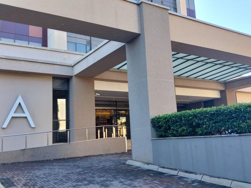 Modern apartment building entrance featuring a covered driveway, concrete pillars, and a paved approach with accessible ramp access.
