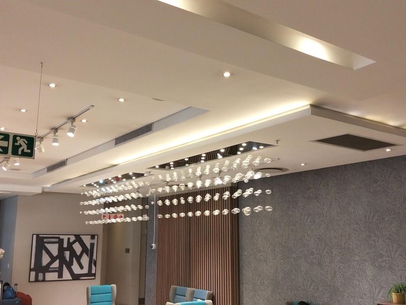 Modern lobby or communal area featuring recessed tray ceilings, integrated downlighting, decorative glass pendant lighting, and textured feature wall paneling.