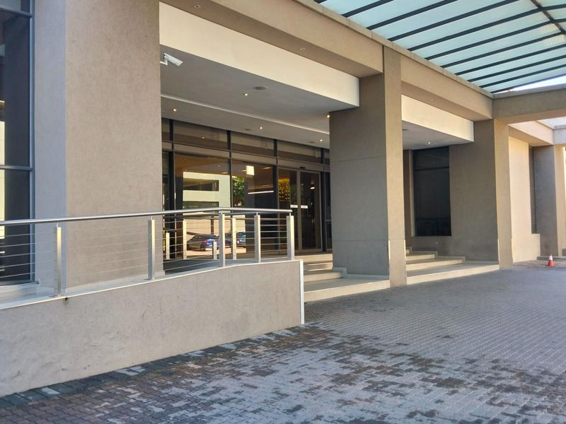 Modern apartment building entrance featuring a covered driveway, glass canopy, and accessible ramp with stainless steel railing.