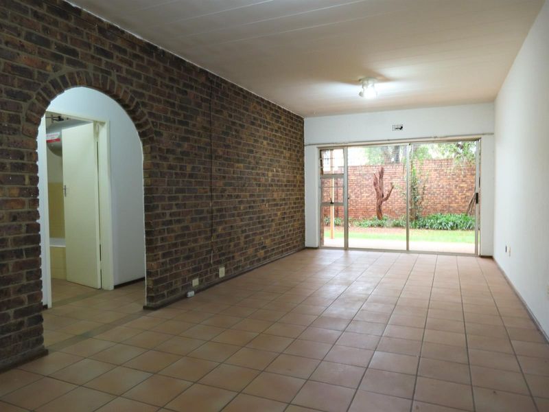 An empty living room featuring an exposed brick feature wall, tiled flooring, and a large sliding glass door providing access to the rear garden.