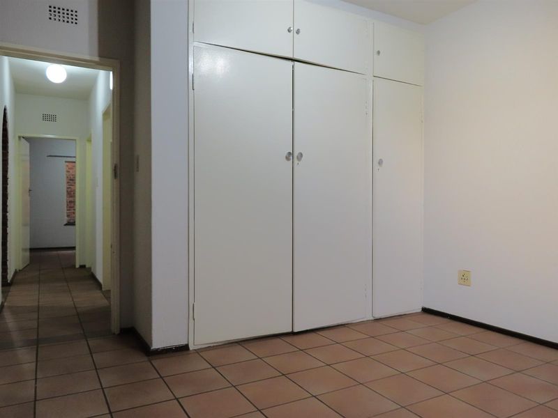 An empty bedroom featuring tiled flooring and white built-in cupboards, with a view into the adjacent hallway.