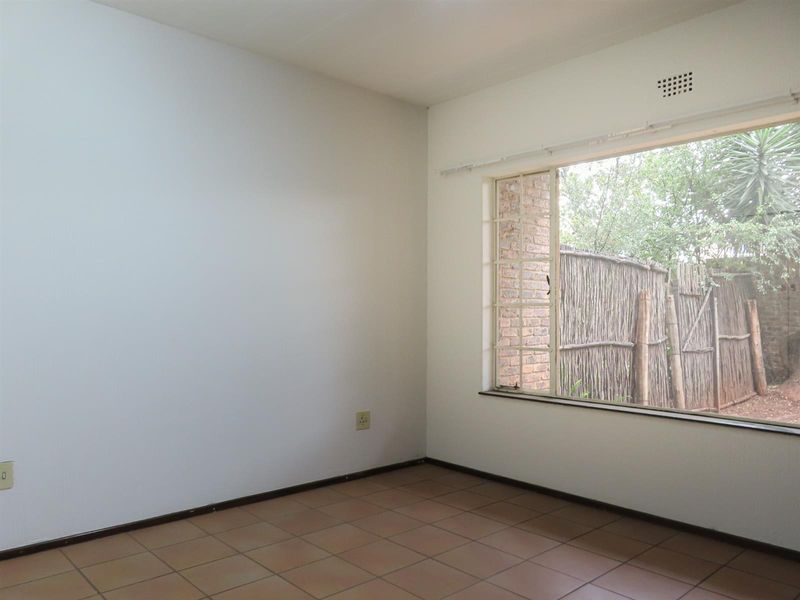 An empty bedroom featuring tiled flooring, a large window with security bars, and neutral wall finishes, offering a blank canvas for personalization.