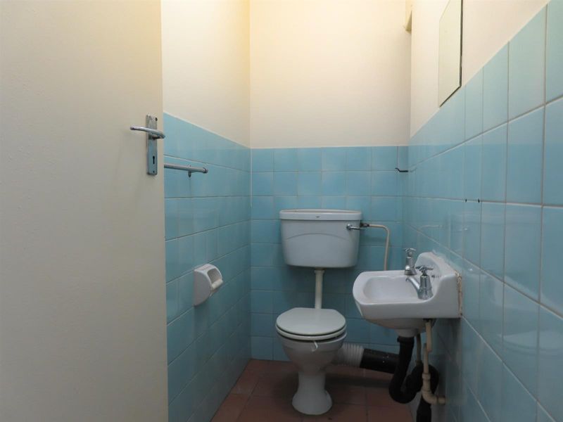 A compact, dated bathroom featuring blue wall tiles, a standard toilet, and a small wall-mounted washbasin with exposed plumbing.