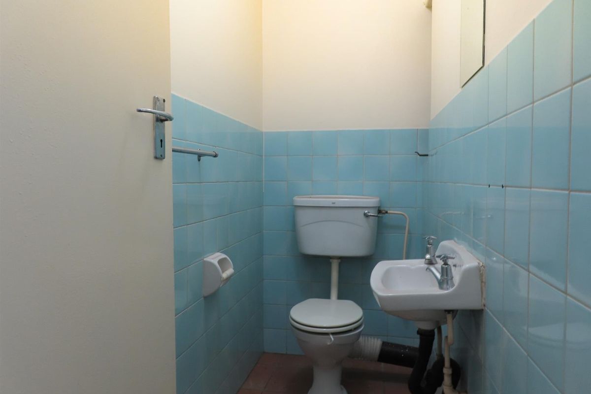 A compact, dated bathroom featuring blue wall tiles, a standard toilet, and a small wall-mounted washbasin with exposed plumbing.