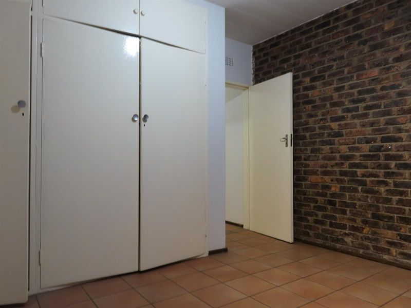 A bedroom featuring built-in cupboards, an exposed brick feature wall, and tiled flooring, offering a neutral canvas for interior design.