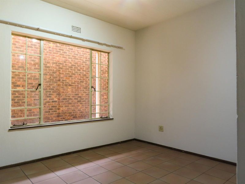 An empty bedroom featuring ceramic tile flooring and a large steel-framed window overlooking a brick wall.