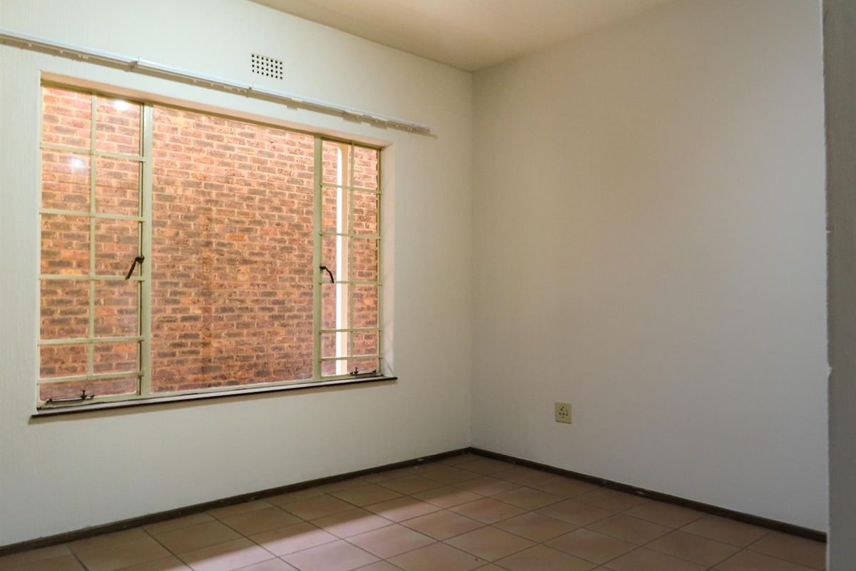An empty bedroom featuring ceramic tile flooring and a large steel-framed window overlooking a brick wall.