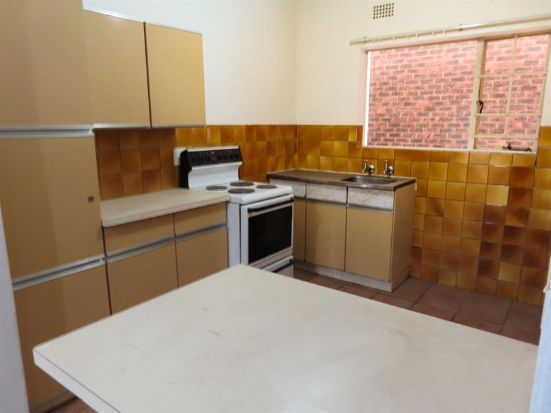 A dated kitchen featuring original cabinetry, a freestanding stove, tiled splashbacks, and a stainless steel sink with a window view.