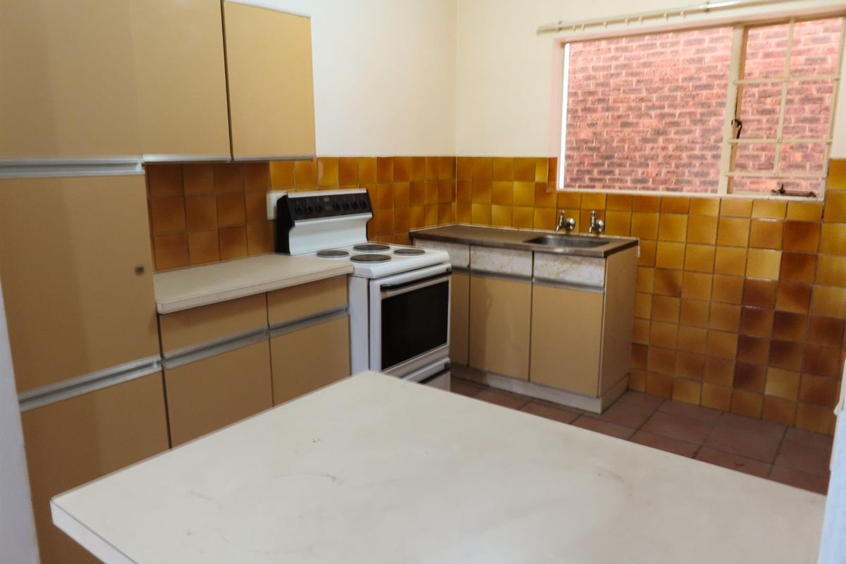 A dated kitchen featuring original cabinetry, a freestanding stove, tiled splashbacks, and a stainless steel sink with a window view.