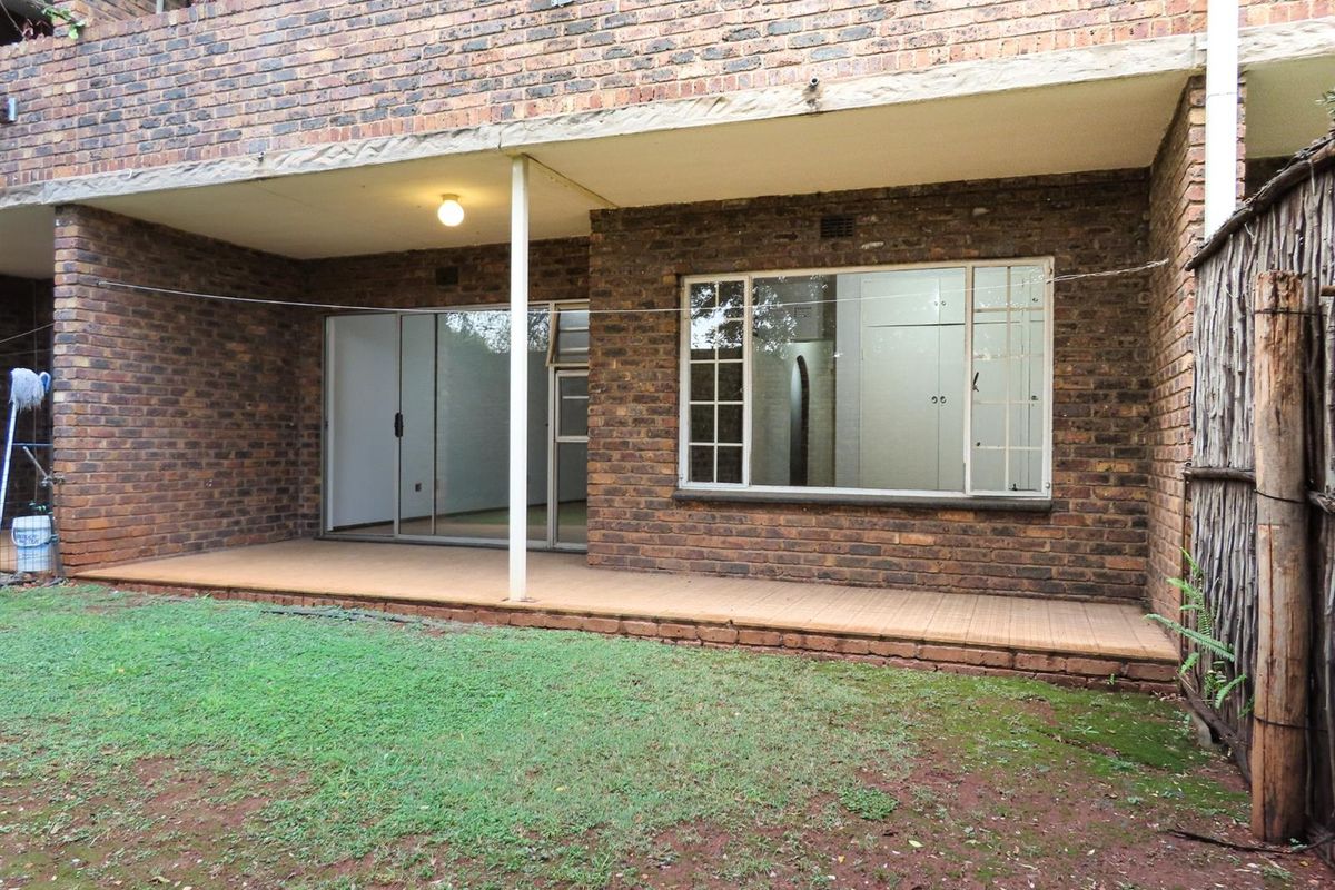 Rear view of the apartment featuring a covered patio area, brick facade, and access to the garden through sliding glass doors.
