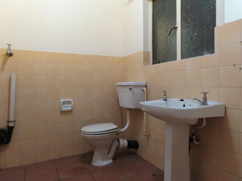 A functional bathroom featuring a pedestal basin, toilet, and dated ceramic wall tiling. The space is vacant and ready for modernization.