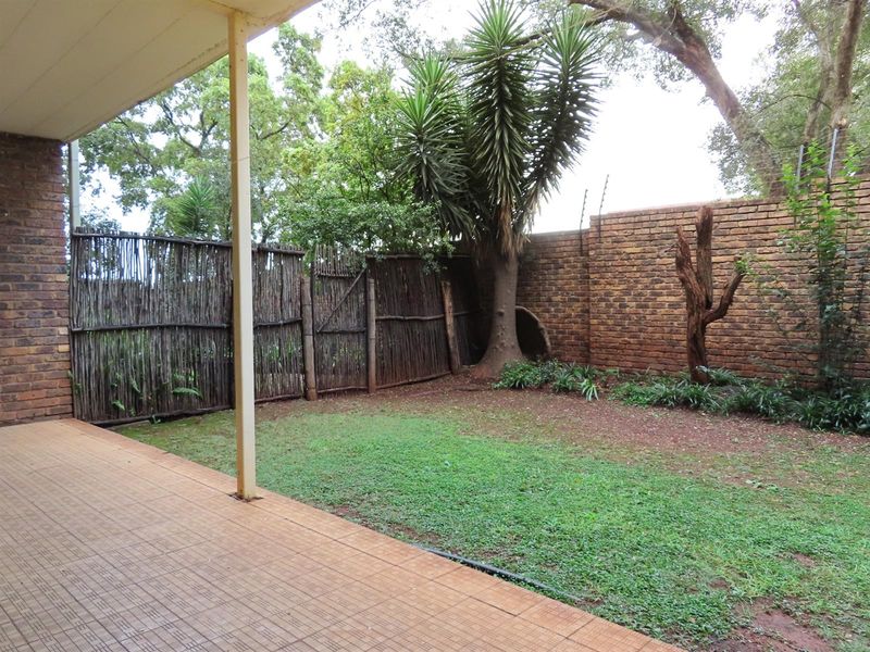 A covered patio area overlooking a private garden with brick boundary walls and rustic wooden fencing.