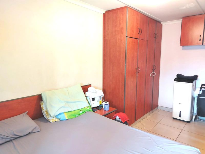 A functional bedroom featuring built-in wooden cupboards and tiled flooring, offering a practical layout with neutral wall finishes.