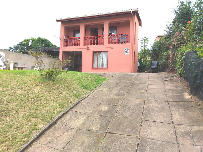 Two-story residential house featuring a paved driveway, front balcony with concrete balustrade, and security bars on windows.
