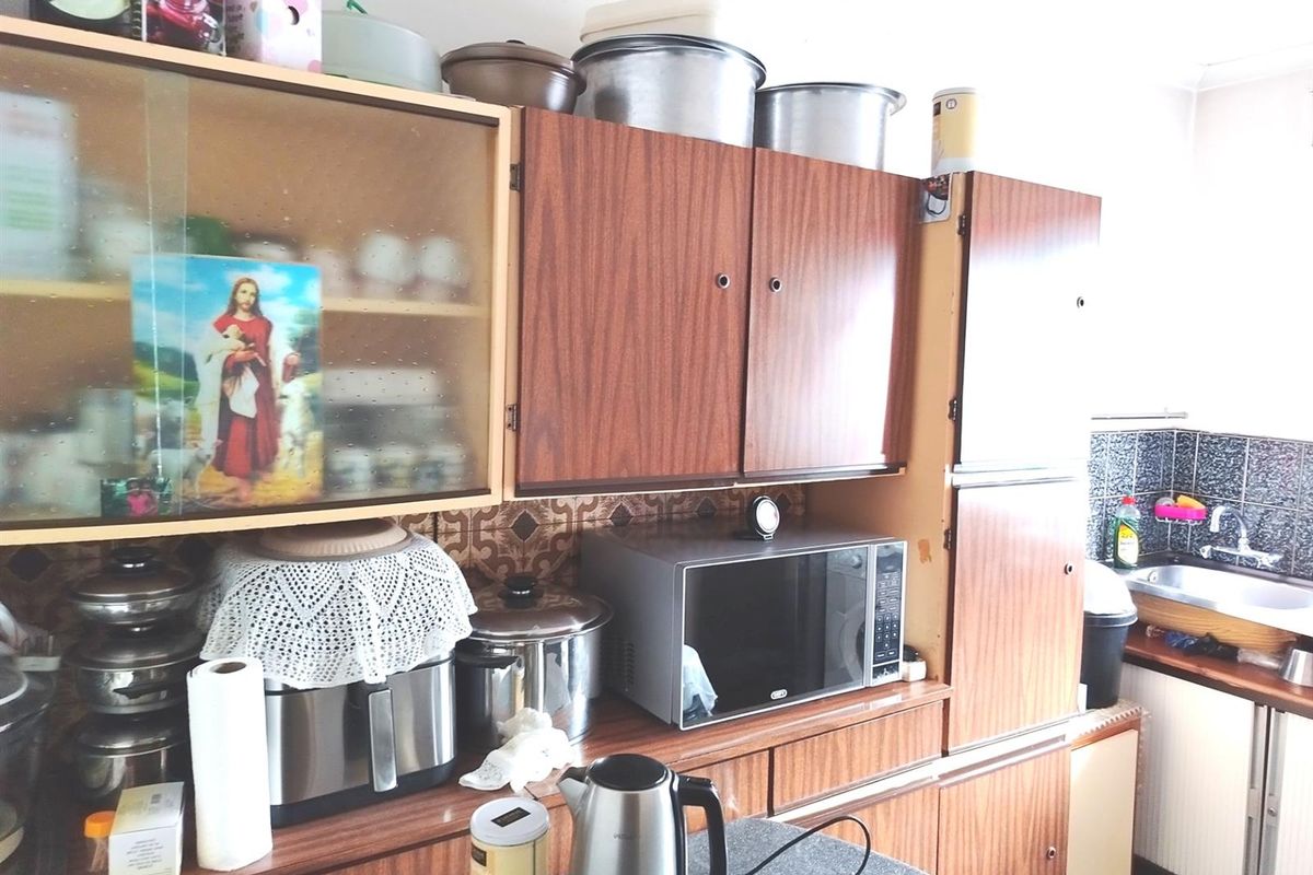 A dated kitchen featuring wood-look laminate cabinetry, a patterned tile backsplash, and a functional stainless steel sink area.