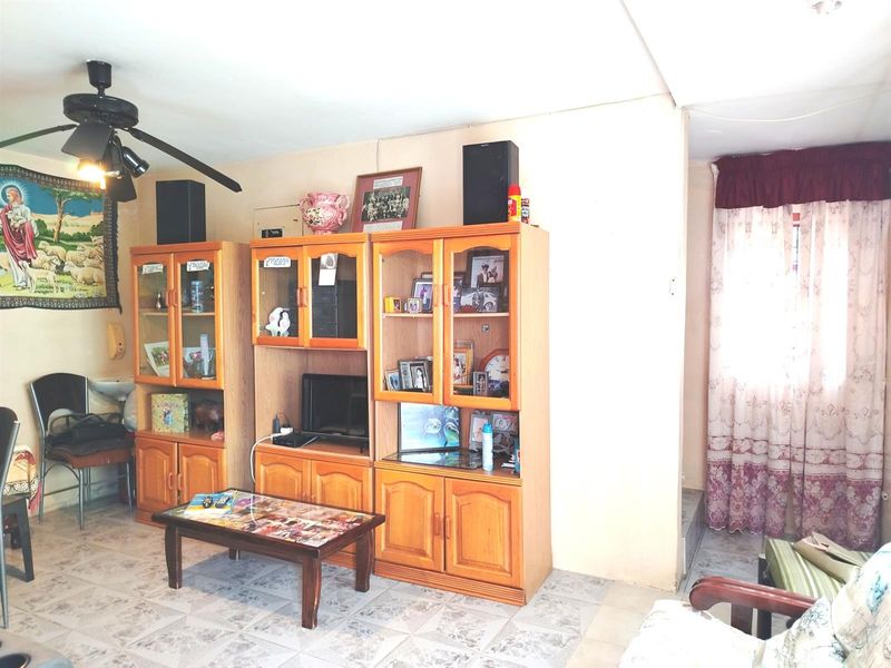 A living room area featuring tiled flooring and a ceiling fan, requiring cosmetic updates to the walls and ceiling to improve the overall aesthetic.