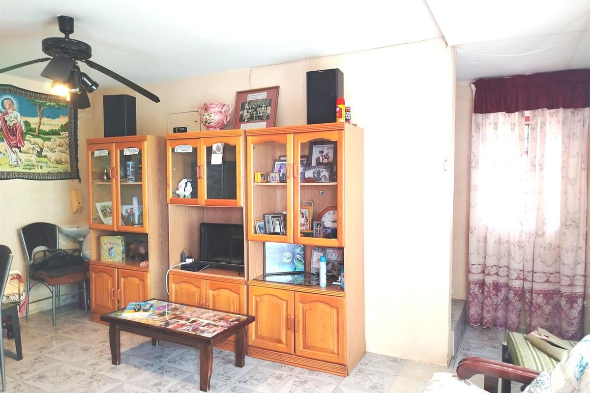 A living room area featuring tiled flooring and a ceiling fan, requiring cosmetic updates to the walls and ceiling to improve the overall aesthetic.