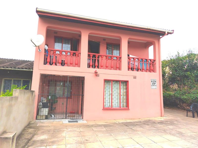 Two-story residential property featuring a covered upper balcony with balustrades, security gates, and a paved front driveway area.