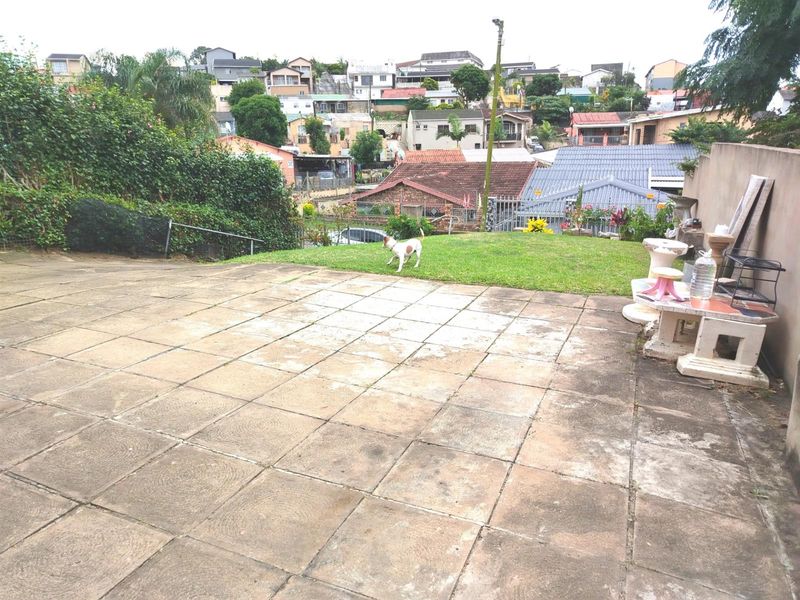 A rear exterior view featuring a paved patio area and a small lawn, overlooking the surrounding residential neighborhood.
