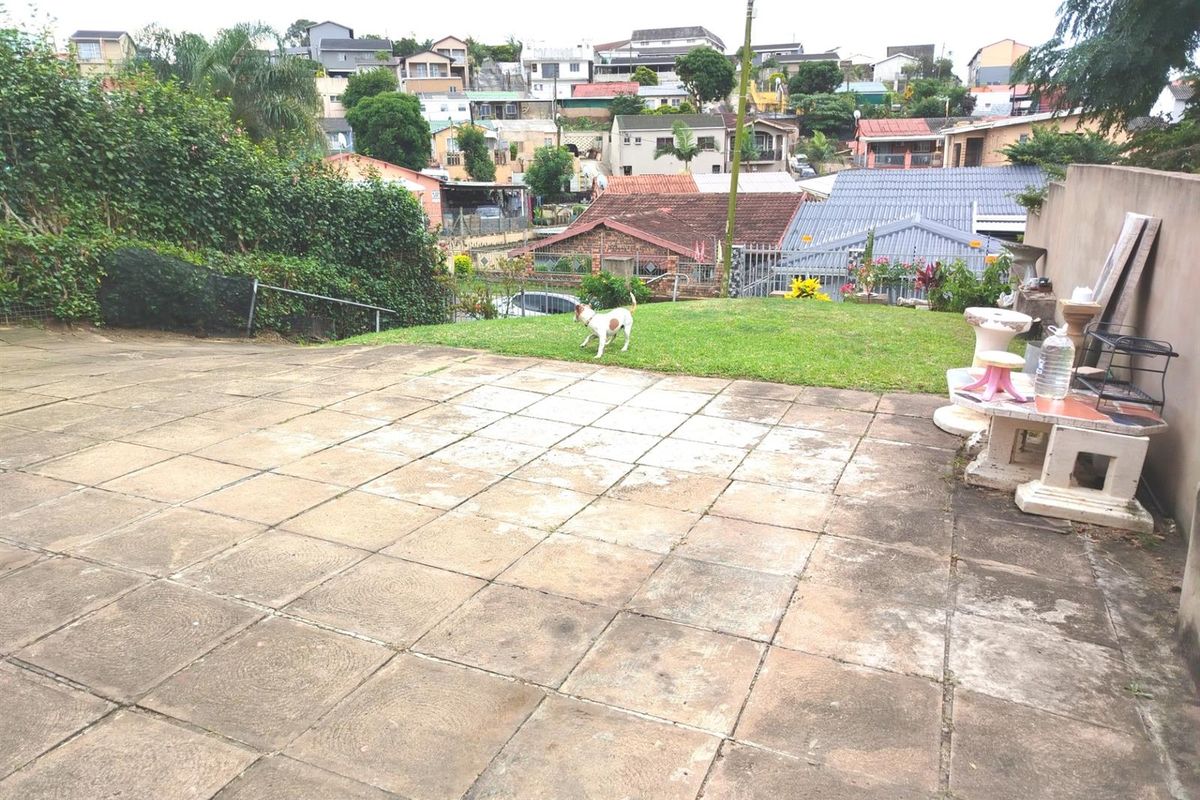 A rear exterior view featuring a paved patio area and a small lawn, overlooking the surrounding residential neighborhood.