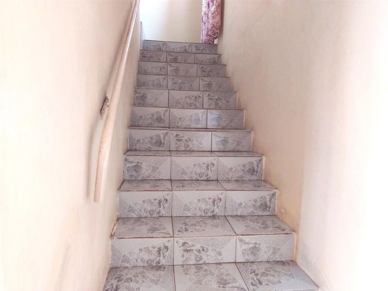 A simple staircase featuring tiled steps and a wall-mounted handrail, showing signs of wear on the surrounding walls.