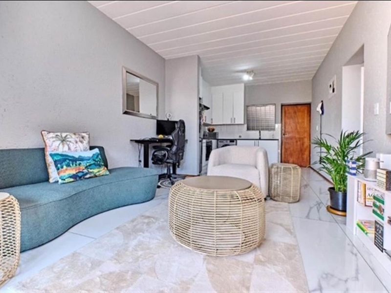 An open-plan living area featuring tiled floors, a compact kitchen with built-in cabinetry, and a neutral color palette throughout the space.