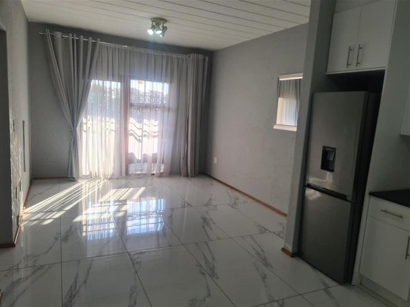 Bright open-plan living and kitchen area featuring modern marble-look floor tiles, neutral walls, and direct access to a balcony through sliding glass doors.