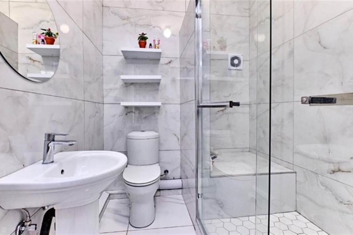 Modern bathroom featuring marble-effect wall tiling, a pedestal washbasin, a glass-enclosed shower, and a toilet.