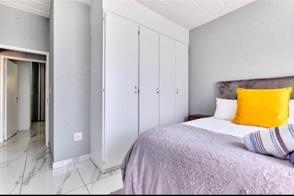 A well-maintained bedroom featuring built-in cupboards, modern white marble-look floor tiles, and neutral grey wall finishes.