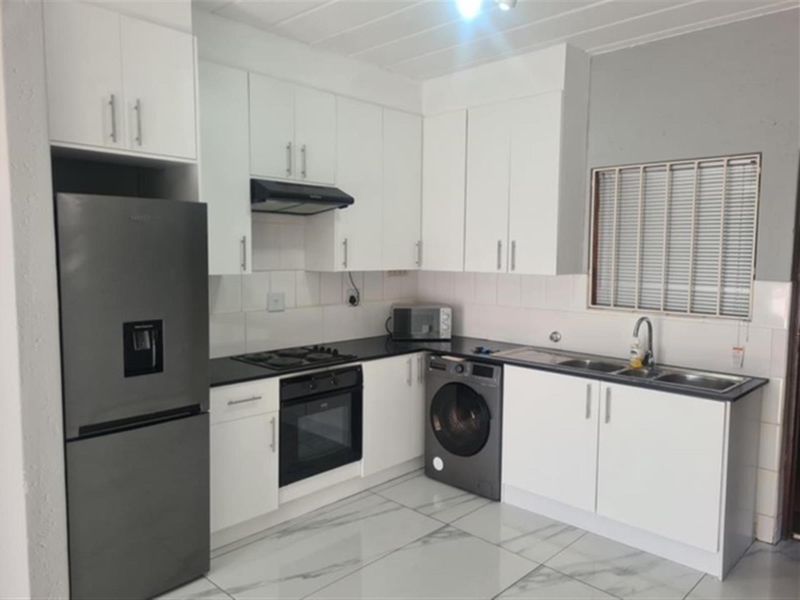 Modern kitchen featuring white cabinetry, black countertops, built-in oven, gas hob, extractor fan, and double sink with tiled flooring.