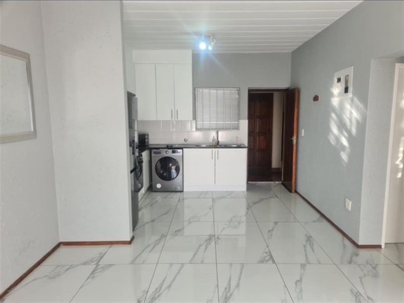 A clean, modern kitchen featuring white cabinetry, marble-look floor tiles, and a tiled backsplash, offering a bright and functional workspace.