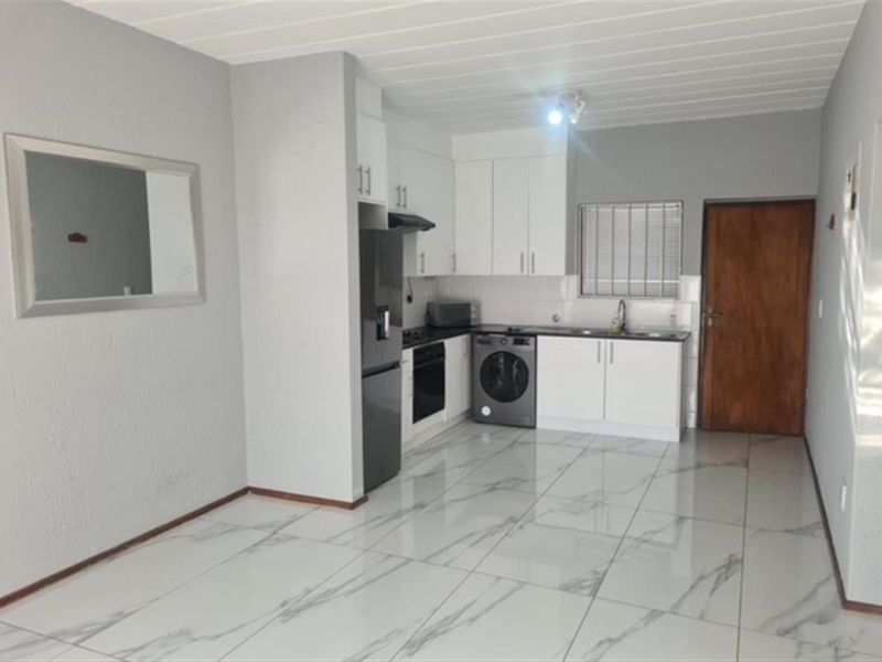 Open-plan kitchen and living area featuring modern white cabinetry, built-in appliances, and polished marble-look tiled flooring.