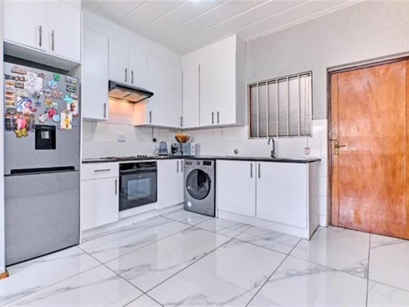 A clean, modern kitchen featuring white cabinetry, built-in oven, hob, extractor fan, and marble-look floor tiles with a functional layout.