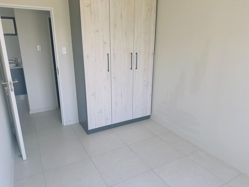 A clean, empty bedroom featuring light-toned tiled flooring and a modern built-in wardrobe with wood-grain finish doors.