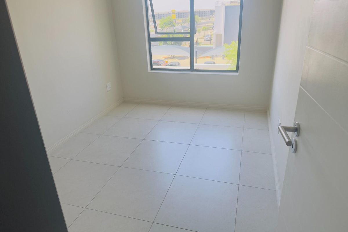 A bright, empty bedroom featuring neutral tiled flooring, clean white walls, and a large window providing natural light and neighbourhood views.