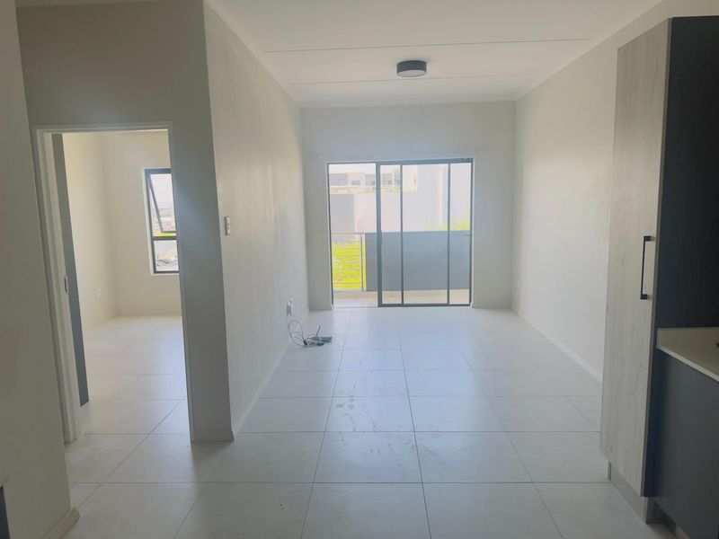 An open-plan living area featuring neutral tiled flooring, built-in cabinetry, and a sliding glass door leading to a private balcony.