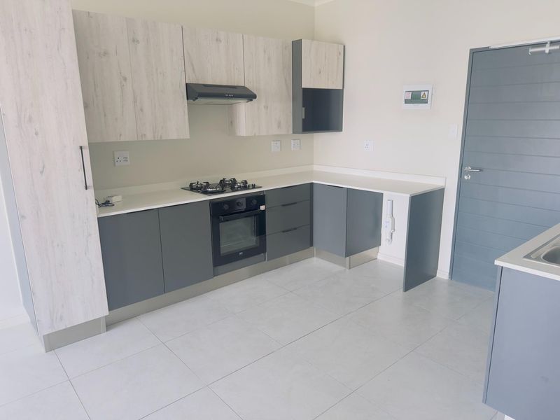 Modern kitchen featuring two-tone cabinetry, stone countertops, built-in gas hob, electric oven, extractor fan, and neutral tiled flooring.