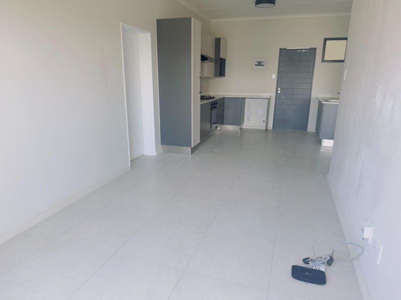 An open-plan living and kitchen area featuring modern grey cabinetry, built-in appliances, and neutral tiled flooring in a clean, vacant space.