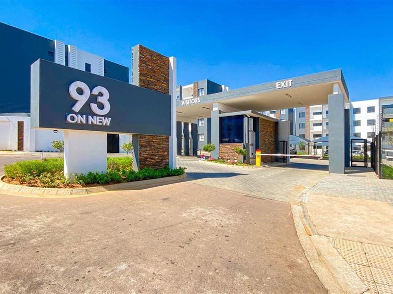 Modern apartment complex entrance featuring a secure gatehouse, stone-clad signage, and paved driveway access.